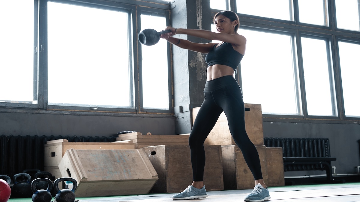 Side View Of Young Beautiful Woman With Perfect Body In Sportswear Working Out With Kettle Bell At Gym.