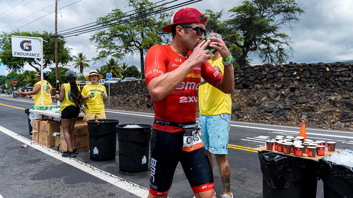 An Elite Male Triathlete Grabbing Several Cups Of Water From An Aid Station During The Kona Race In 2022