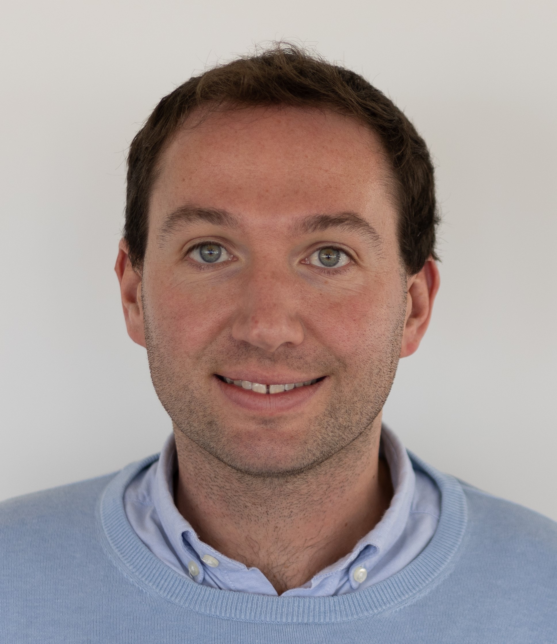 Dr. Will Hicks, Smiling And Wearing A Light Blue Collared Shirt Under A Light Blue Sweater.