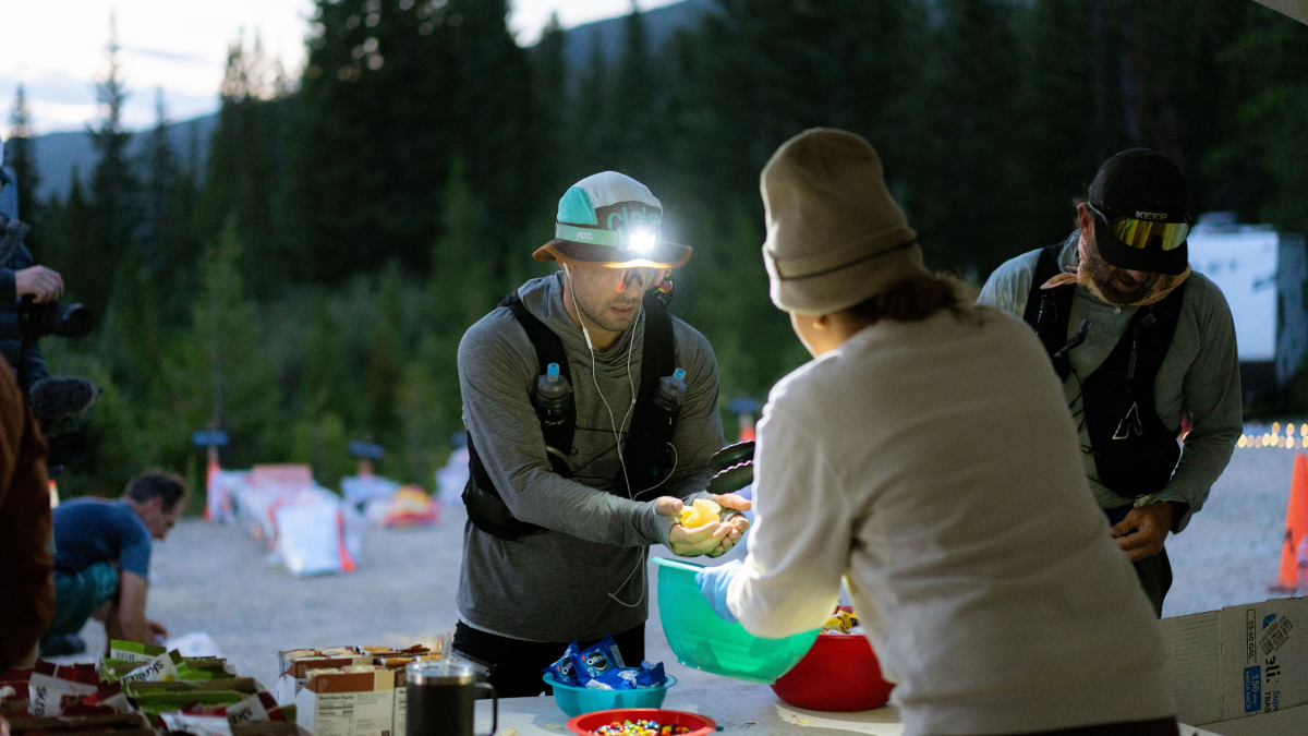 Man Wearing A Running Hat And Vest, Getting Orange Slices From A Race Station—and Excellent Source Of Gluten Free Carbohydrates.