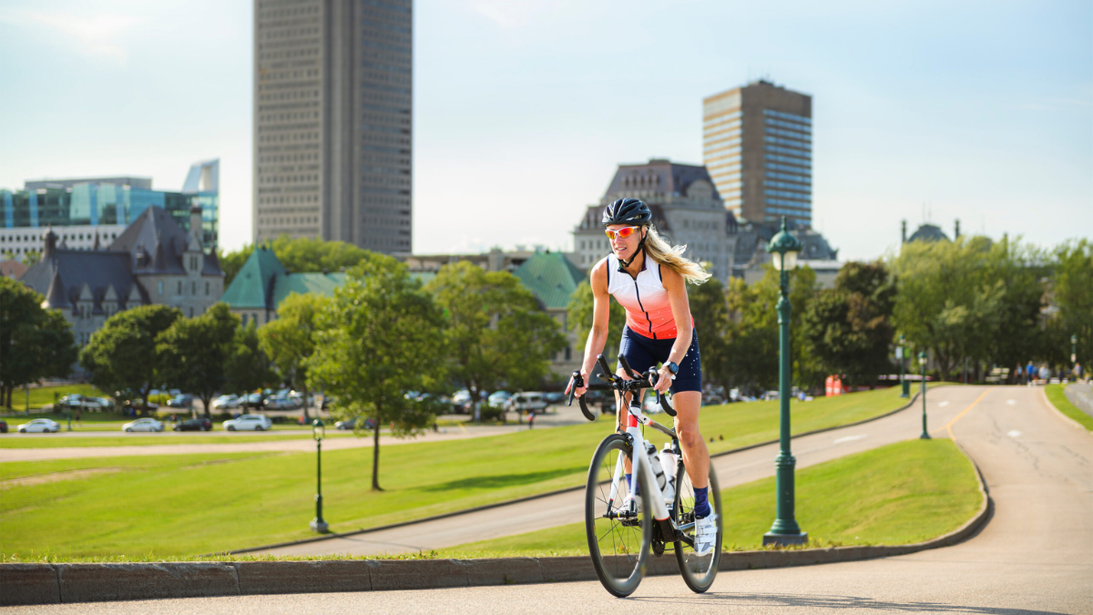 Female Cyclists On Bike Cycling Outside With City In Background